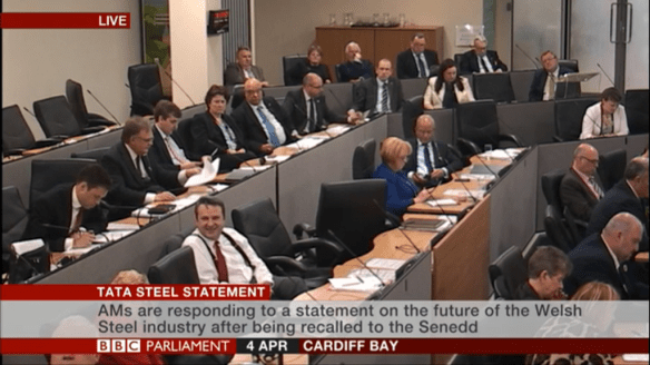 A small beige room with four rows of people behind wooden desks.